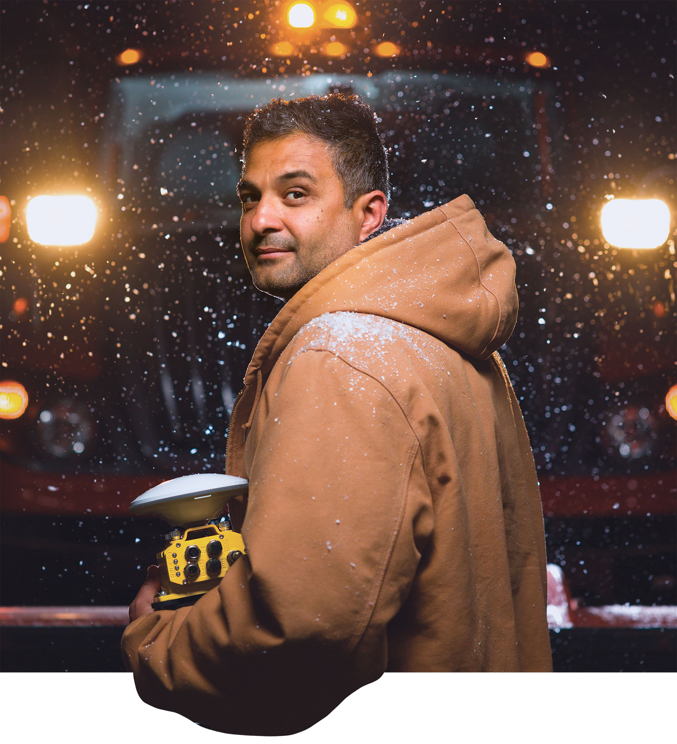 Anuj Sharma in winter coat posing in front of snowplow on a dark snowy night.